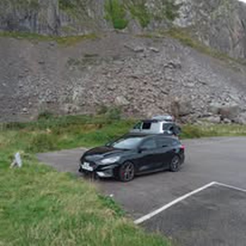 Black private hire car parked below the cliffs